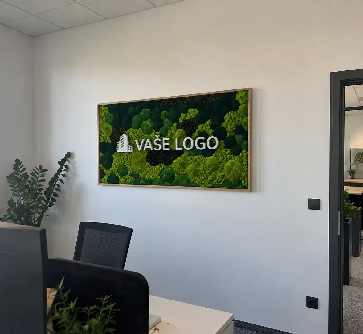 Vizualizácia machového obrazu Verdara s bielym nápisom „VAŠE LOGO“ v drevenom ráme na svetlej stene pri pracovnom stole.